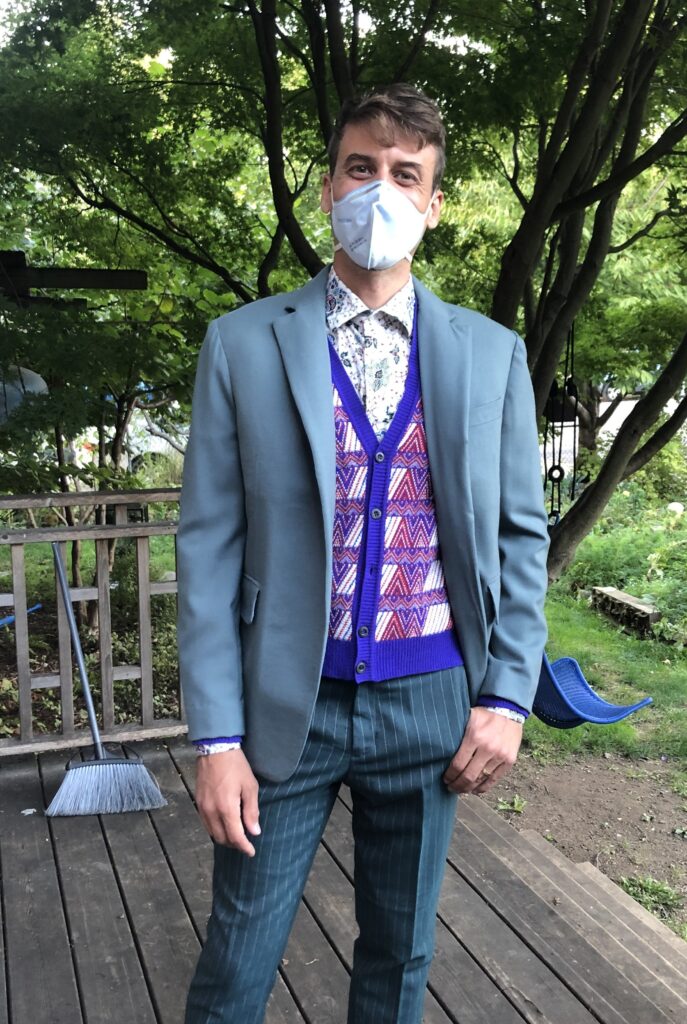 My son, Greg, is pictured in the suit jacket I tailored for the celebration of commitment he and his partner hosted. The jacket is medium grey-green wool. He wears it with a bright multi-colored knitted vest and pants of a darker grey-green with a thin stripe that matches the color of the jacket.